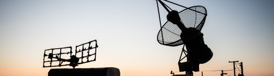 Creative artwork decoration. Silhouette of mobile air defence truck with radar antenna during sunset. Satellite dishes or radio antennas against evening sky. Selective focus