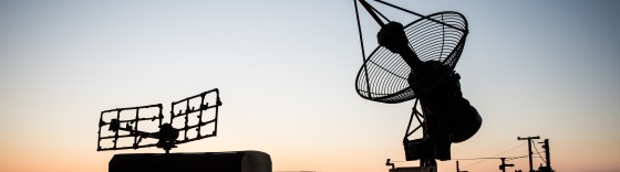 Creative artwork decoration. Silhouette of mobile air defence truck with radar antenna during sunset. Satellite dishes or radio antennas against evening sky. Selective focus